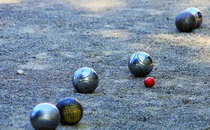 Mehrere Metallkugeln und eine kleine rote Kugel auf einem Sandplatz beim Boule-Spiel