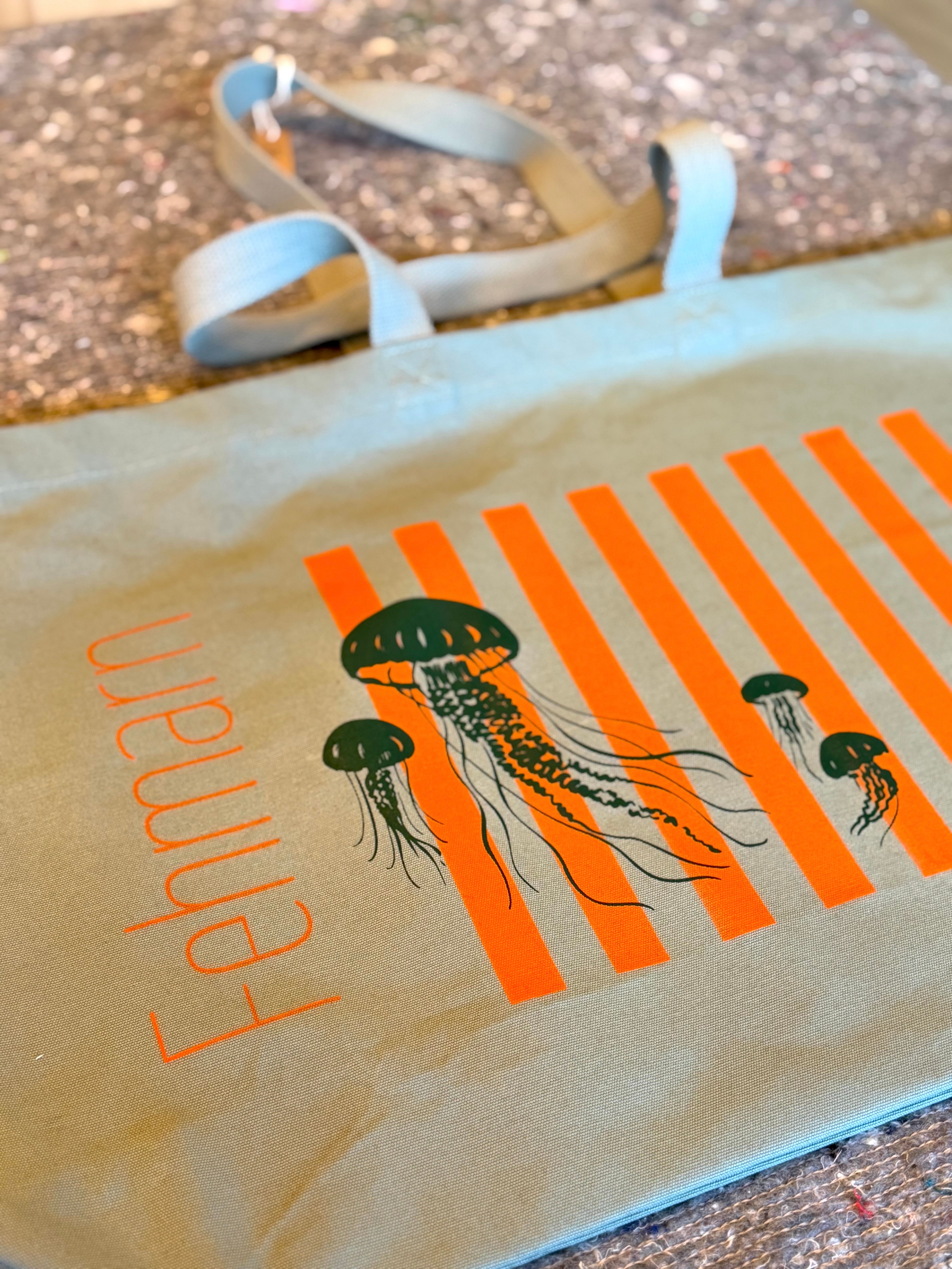 Stofftasche mit dem Aufdruck 'Fehmarn' und einem Design aus Quallen und orangen Streifen auf einem Tisch liegend.