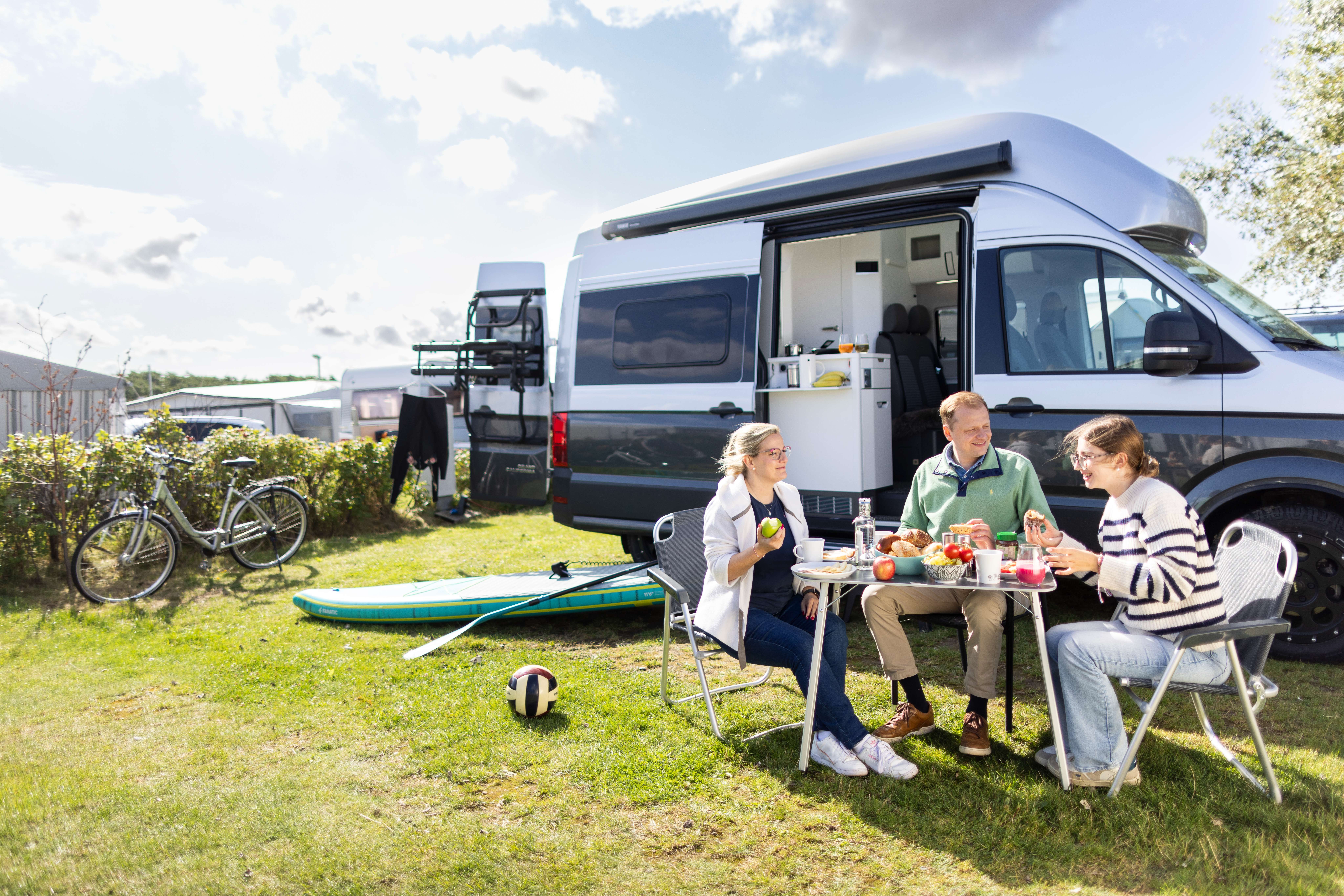 Familie sitzt vor ihrem Camper und frühstückt