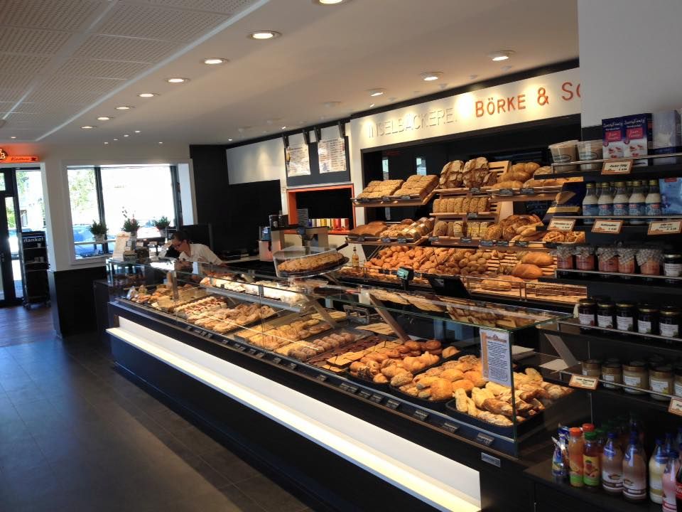 Eine gut sortierte Bäckerei mit frischen Backwaren und Produkten in Regalen und Vitrinen. Ein Mitarbeiter steht hinter der Theke.