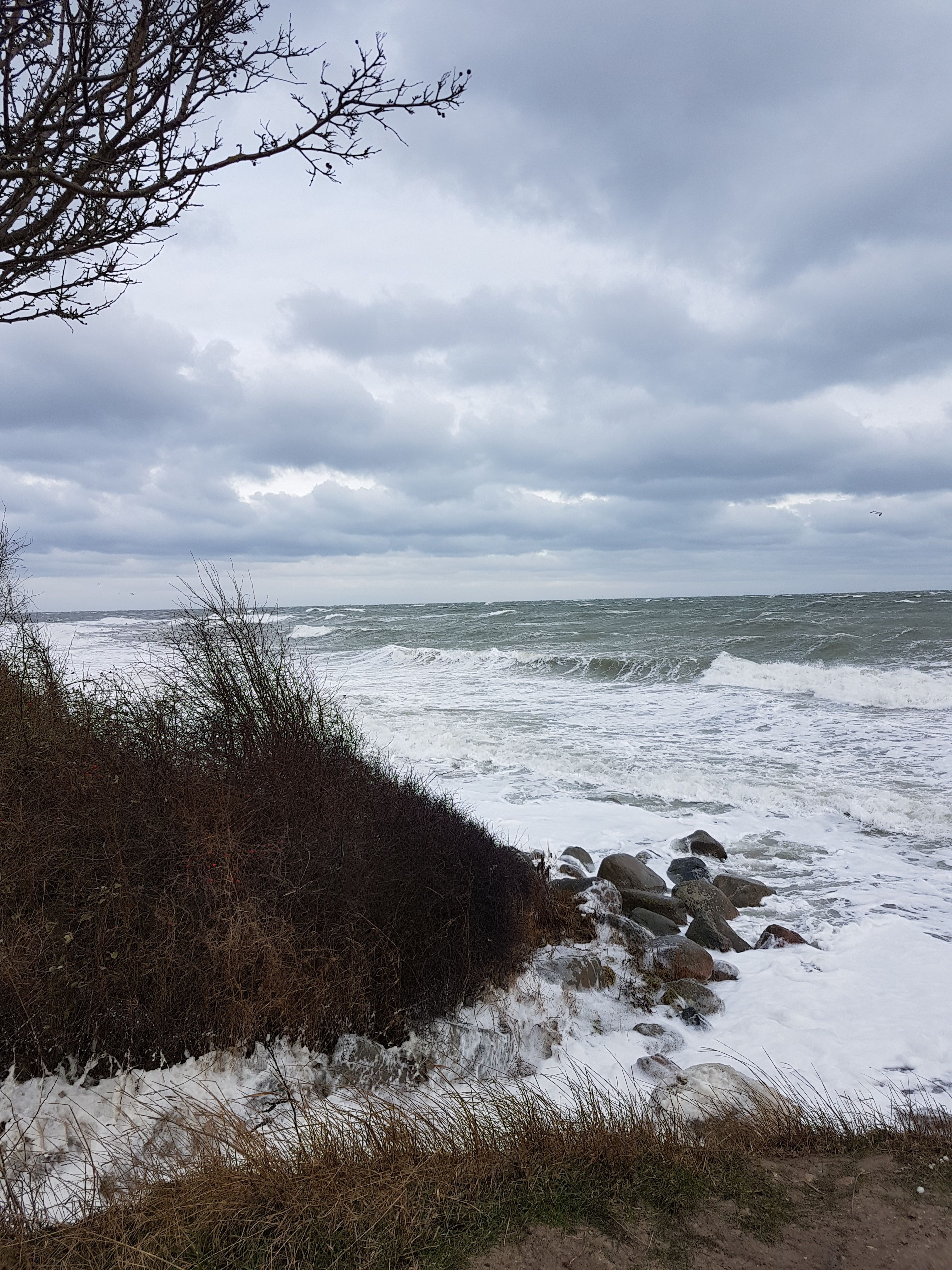 Stürmische See bei Staberdorf mit hohen Wellen, die gegen das Ufer schlagen. Der Himmel ist bewölkt und die Vegetation am Ufer ist karg.
