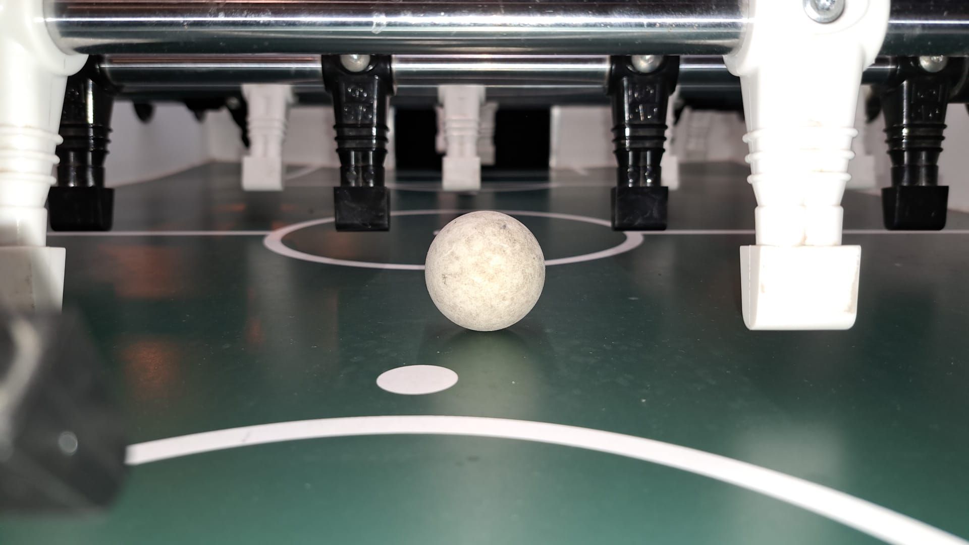 Nahaufnahme beim Kickerturnier: Ein weißer Ball liegt auf dem Spielfeld zwischen schwarzen und weißen Tischkicker-Figuren.