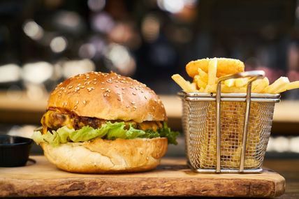 Ein saftiger Burger mit Salat und Käse, serviert neben knusprigen Pommes in einem Metallkorb auf einem Holzbrett.