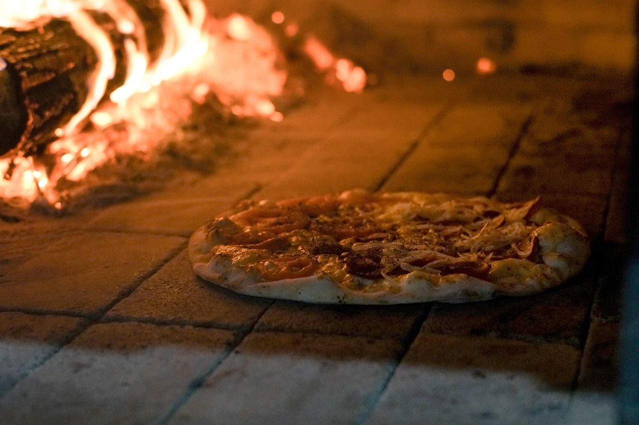 Eine Pizza wird in einem traditionellen Holzofen gebacken, umgeben von Flammen und glühenden Holzscheiten.