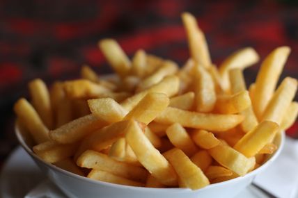 Eine Schüssel voller knuspriger, goldbrauner Pommes frites. Der Hintergrund ist unscharf und dunkel gehalten.