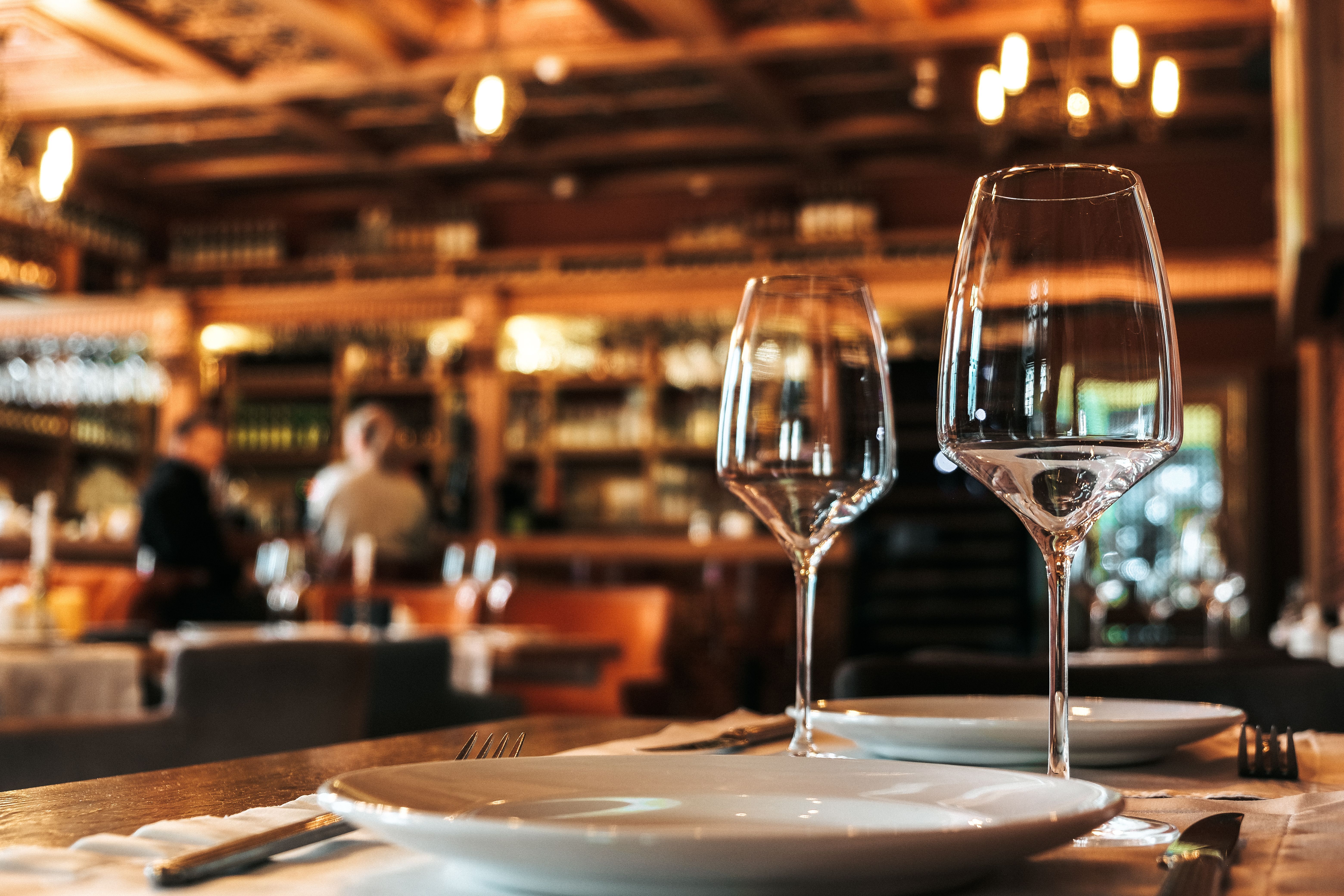 Ein stilvoll gedeckter Tisch in einem Restaurant mit Weingläsern und Tellern, im Hintergrund eine unscharfe Bar.