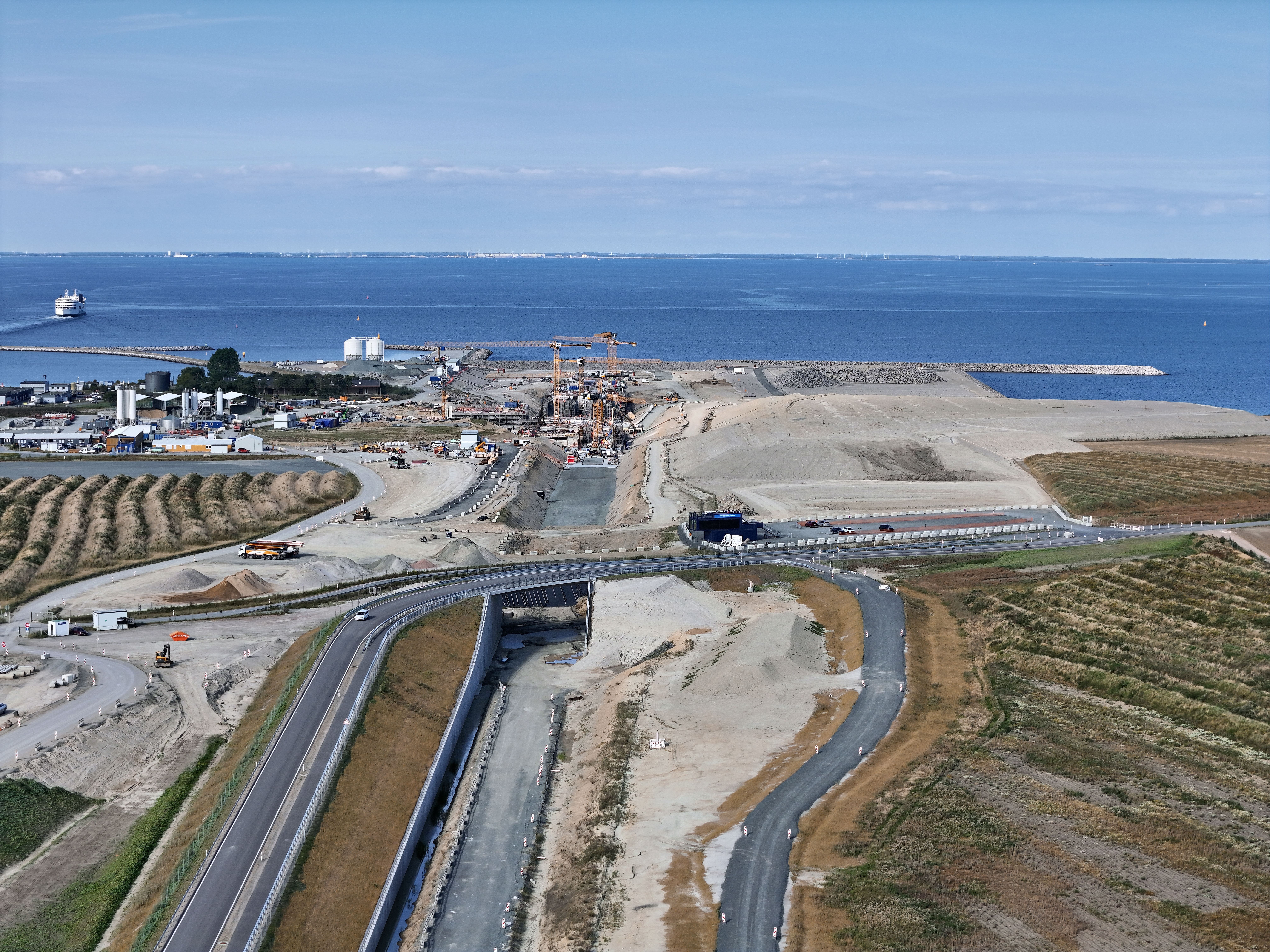 Luftaufnahme der Tunnelbaustelle Puttgarden mit Baukränen, Baumaschinen und Hafenanlage an der Küste der Ostsee.