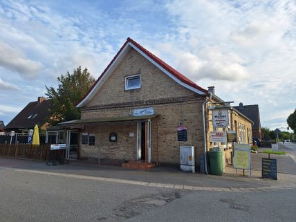 Ein Backsteingebäude mit rotem Dach beherbergt Dieter's Grill in Landkirchen, Fehmarn. Vor dem Gebäude stehen Schilder mit Speiseangeboten.