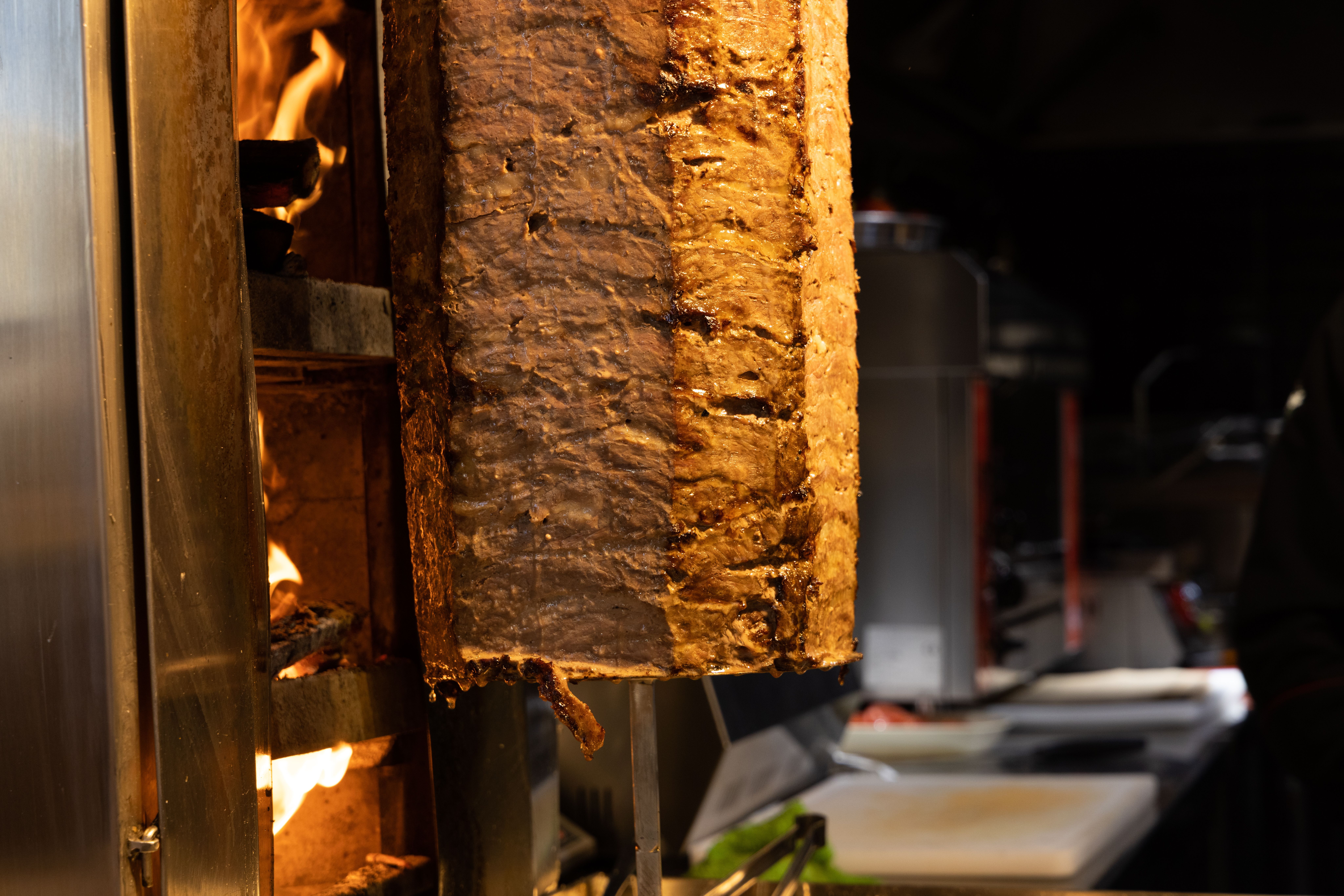 Ein Döner-Spieß dreht sich vor einem offenen Feuer in einer Küche. Das Fleisch ist goldbraun und saftig.