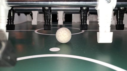 Nahaufnahme beim Kickerturnier: Ein weißer Ball liegt auf dem Spielfeld zwischen schwarzen und weißen Tischkicker-Figuren.