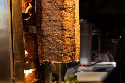 Ein Döner-Spieß dreht sich vor einem offenen Feuer in einer Küche. Das Fleisch ist goldbraun und saftig.