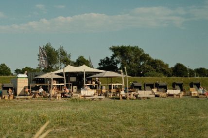 Die Strandbar Strukkamp bietet eine entspannte Atmosphäre mit Sonnensegeln und Sitzgelegenheiten im Freien, umgeben von grüner Landschaft.