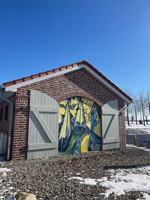 Ein Backsteingebäude mit einem bemalten Tor, das ein expressionistisches Kunstwerk zeigt. Der Boden ist mit Schnee bedeckt, und der Himmel ist klar und blau.