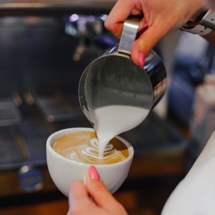 Nahaufnahme von Latte Art: Eine Hand gießt Milch in eine Kaffeetasse und kreiert ein Muster.