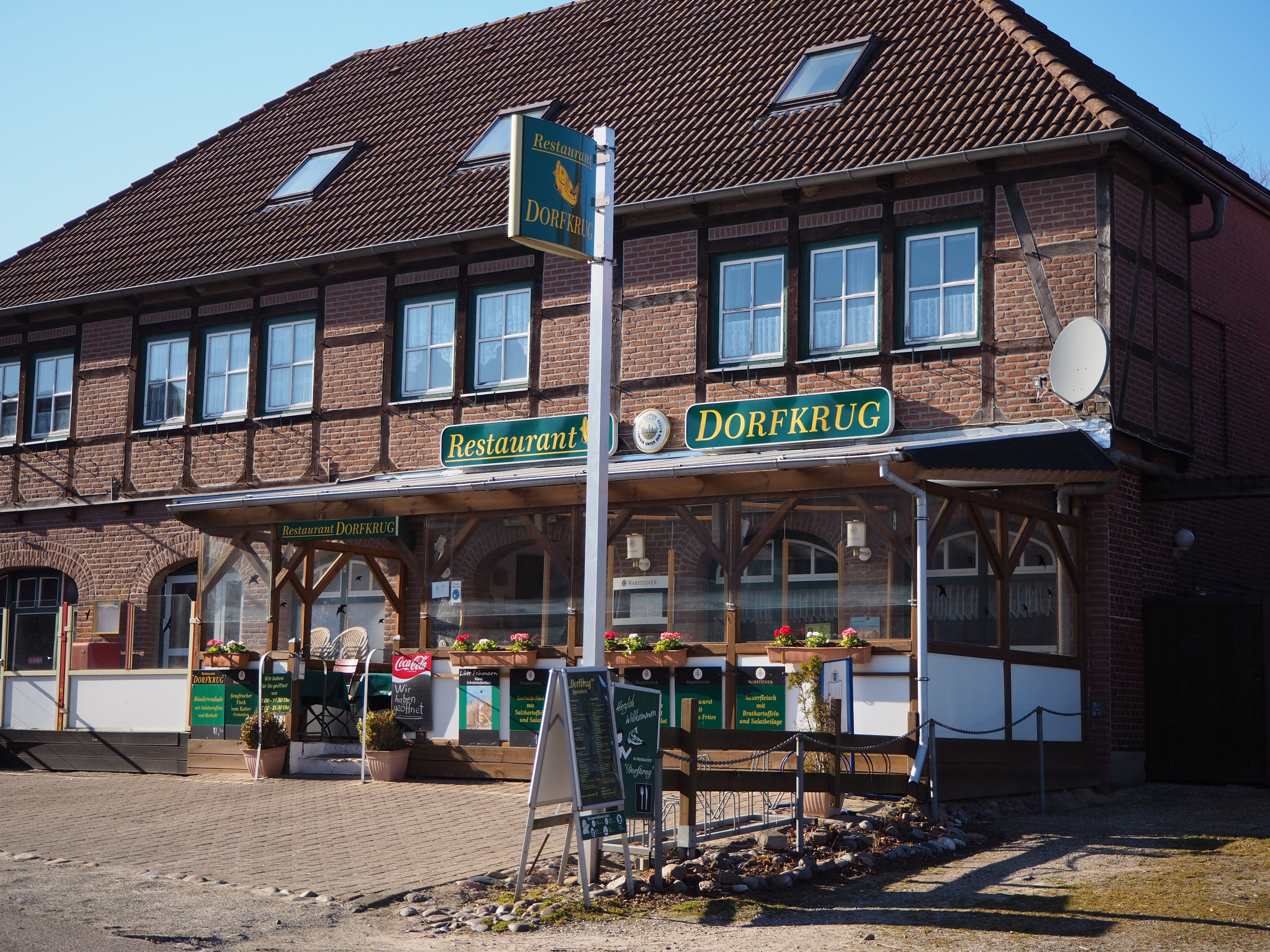 Ein traditionelles Restaurant namens 'Dorfkrug' in einem Backsteingebäude mit Holzelementen und Blumendekorationen.