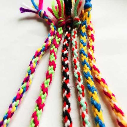 Bunte, geflochtene Kordeln aus Wolle in verschiedenen Farben und Mustern auf weißem Hintergrund.