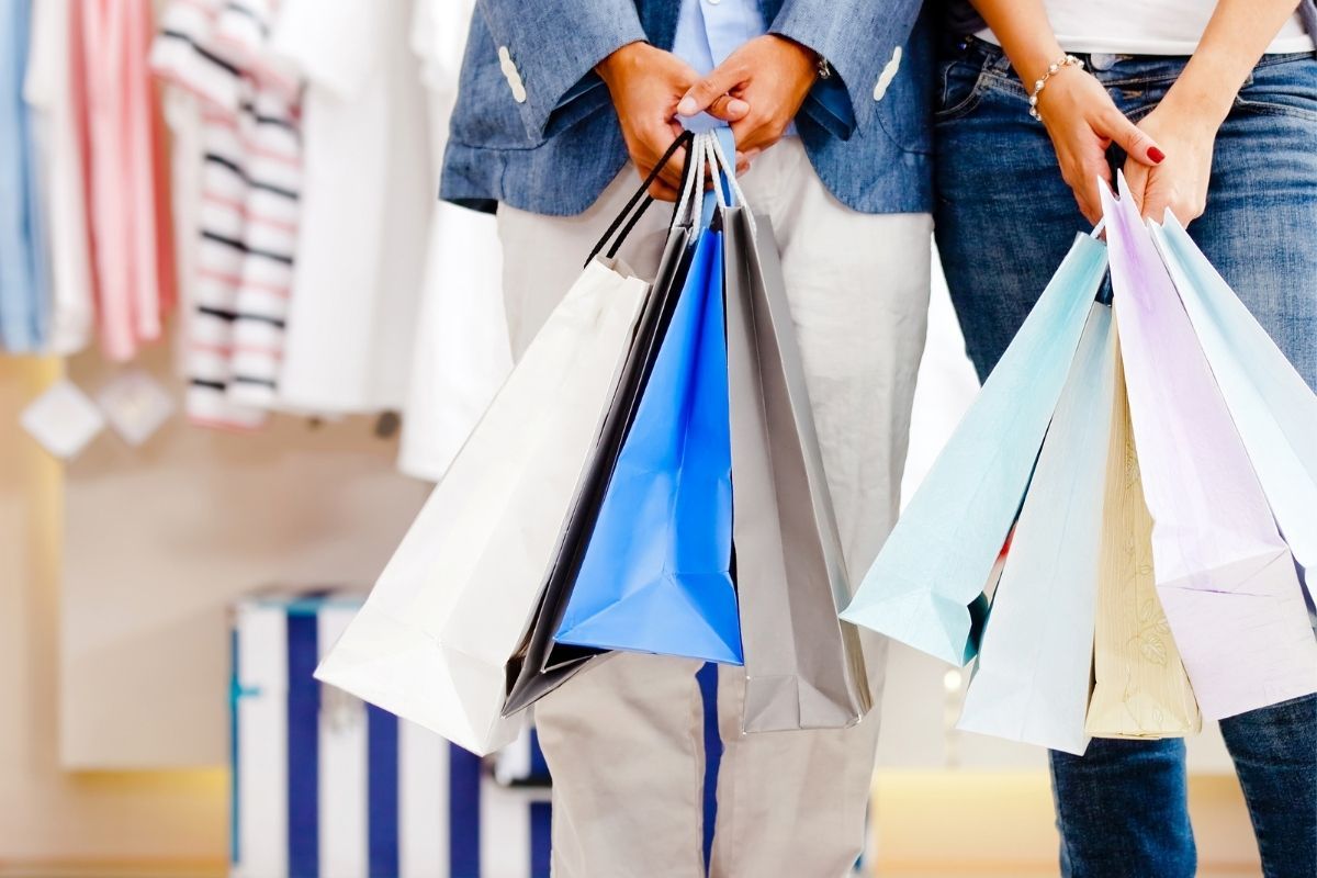 Zwei Personen stehen nebeneinander und halten bunte Einkaufstüten in einem Bekleidungsgeschäft.
