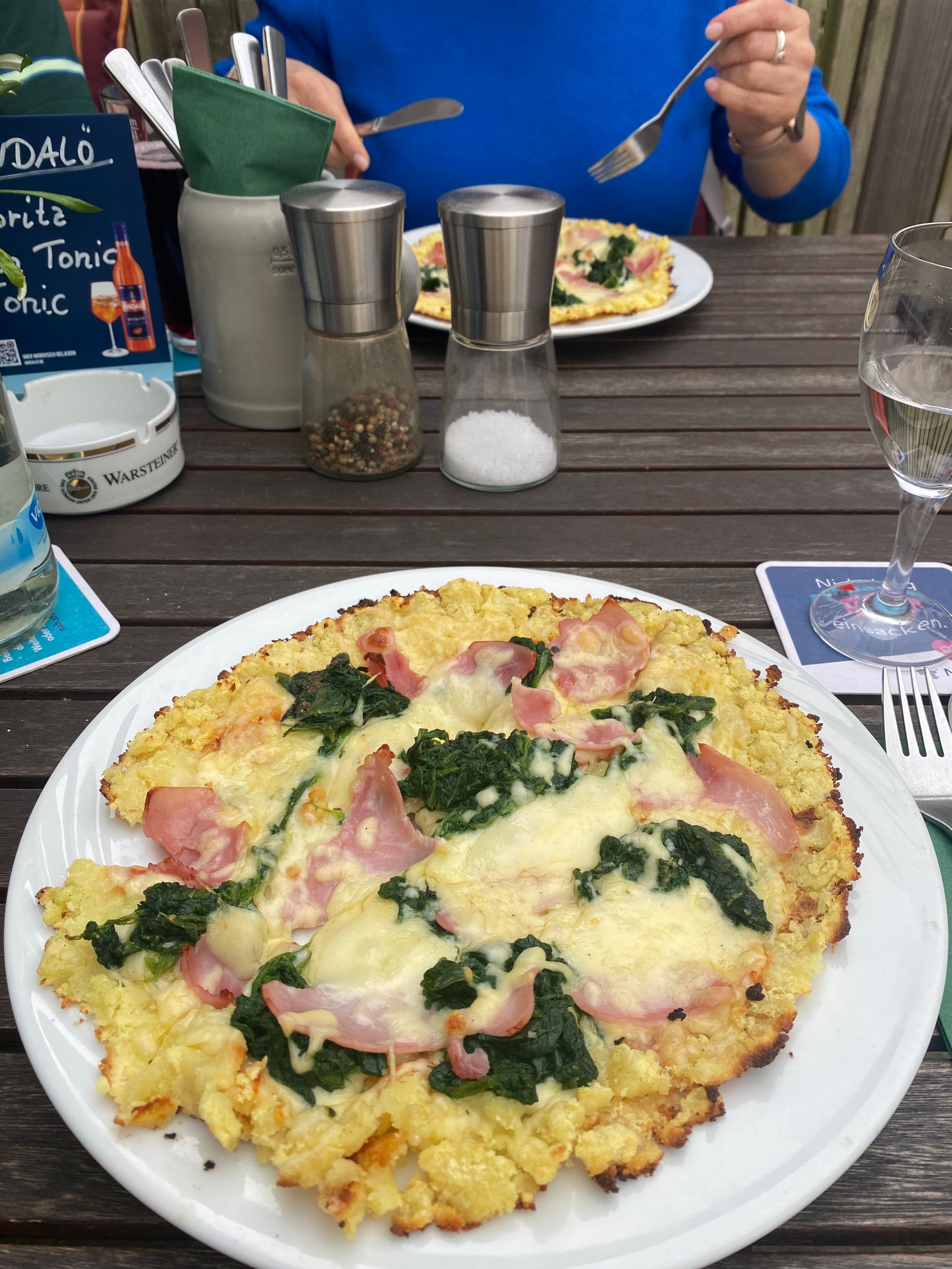 Kartoffel-Pizza mit Schinken, Spinat und Käse auf einem Holztisch. 