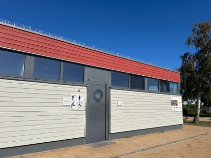 Öffentliches Toilettengebäude mit rotem und grauem Anstrich, Schilder für barrierefreie Toiletten.