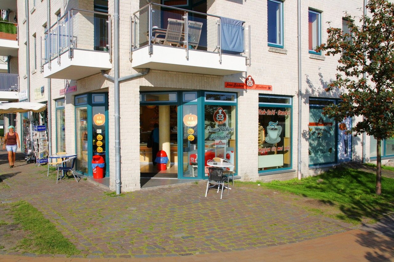 Die Inselbäckerei Börke & Sohn in Burgtiefe zeigt einen einladenden Eingang mit großen Fenstern und einem kleinen Tisch im Freien. Ein sonniger Tag.