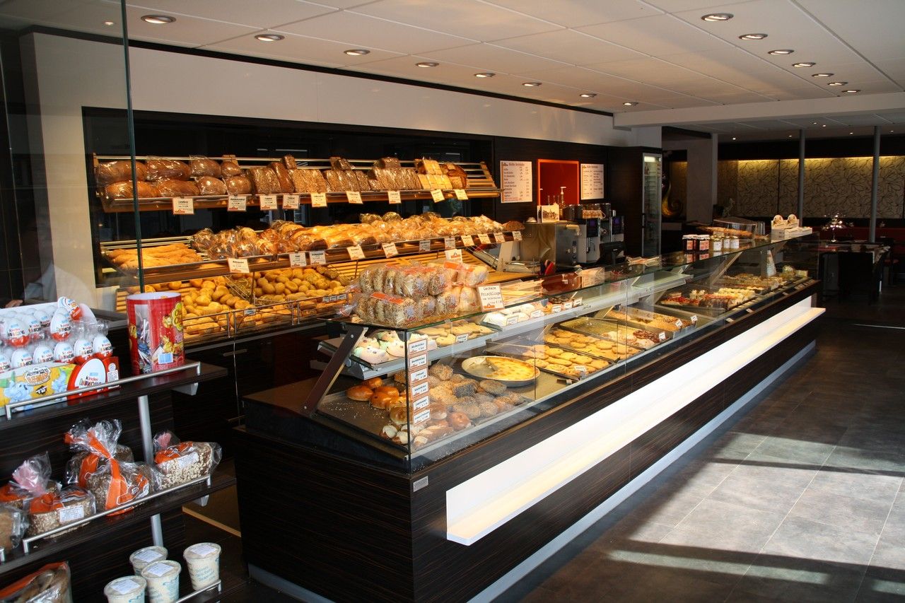 Eine Bäckerei mit reichhaltiger Auswahl an Broten, Brötchen und Gebäck in der Auslage. Die Theke ist gut beleuchtet und ordentlich arrangiert.