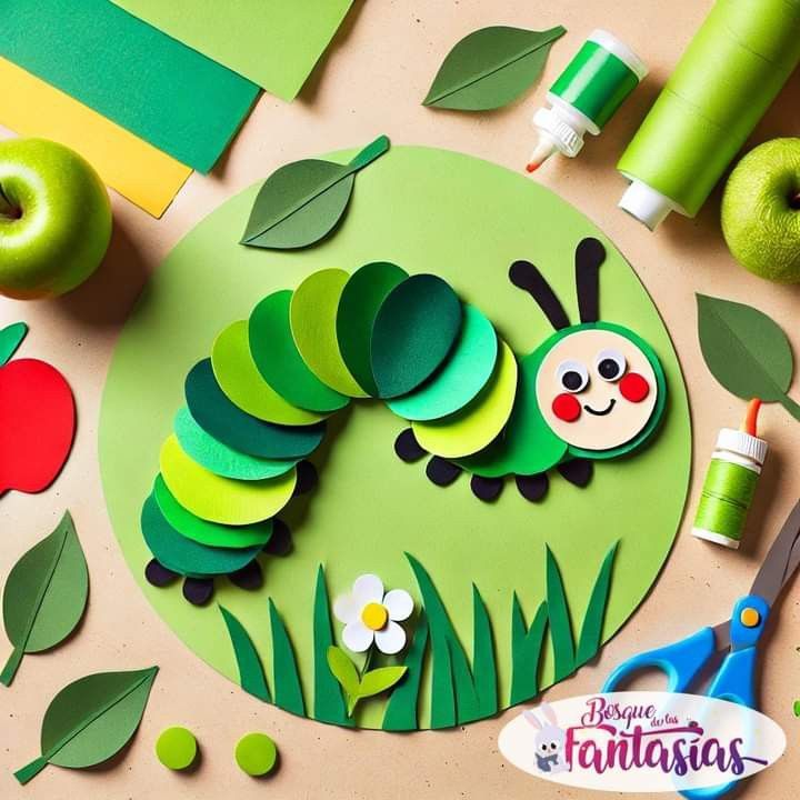 Bunte Bastelarbeit einer Raupe aus Papier, umgeben von grünen Blättern, Äpfeln und Bastelmaterialien auf einem Tisch.