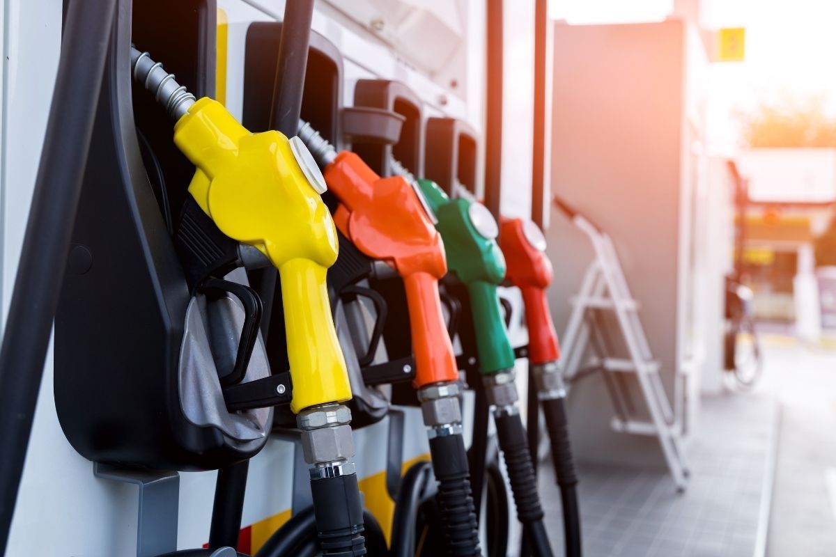 Zapfpistolen in Gelb, Rot, Grün und Schwarz an einer Tankstelle. Sonnenlicht im Hintergrund.