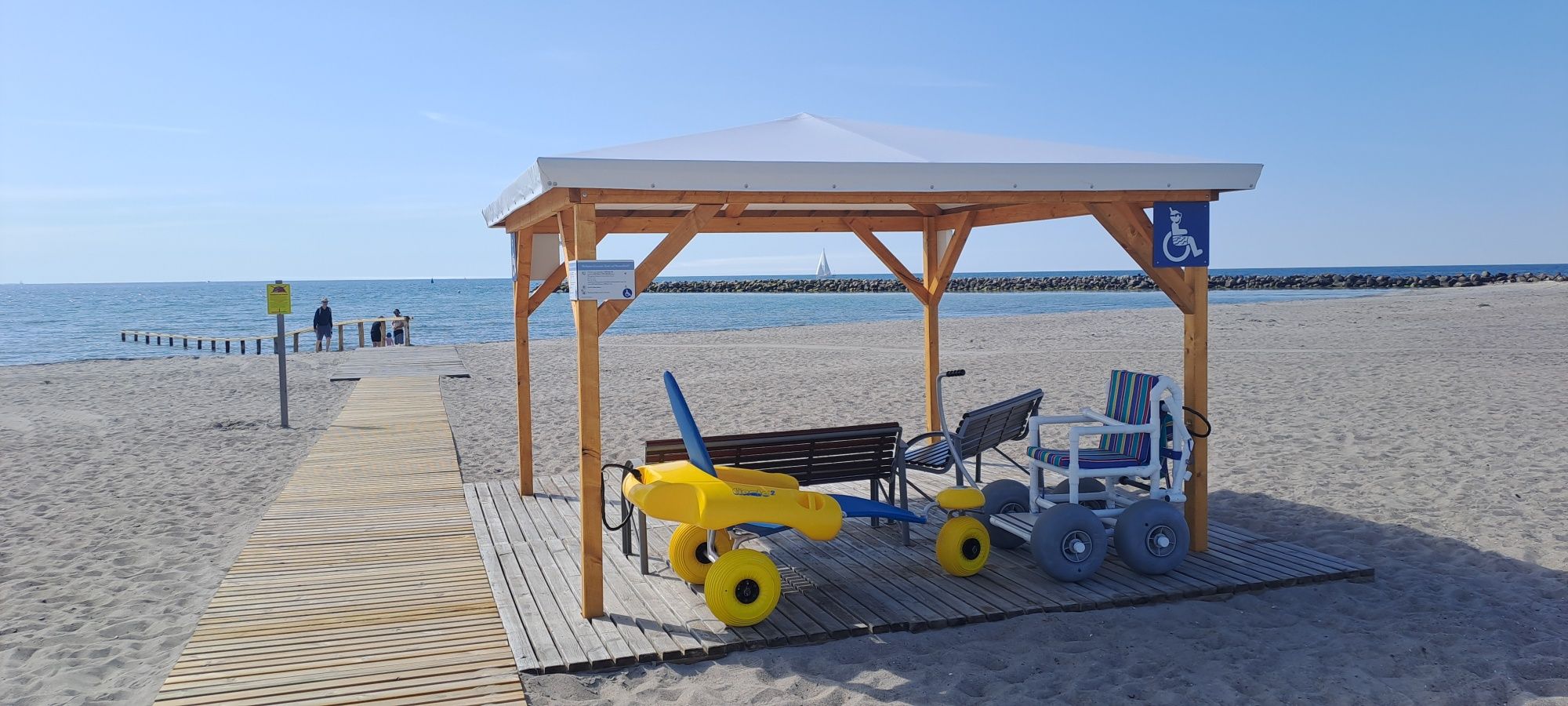 Ein barrierefreier Strandbereich mit Holzsteg und Spezialrollstühlen. Der Zugang zum Meer ist behindertengerecht gestaltet.