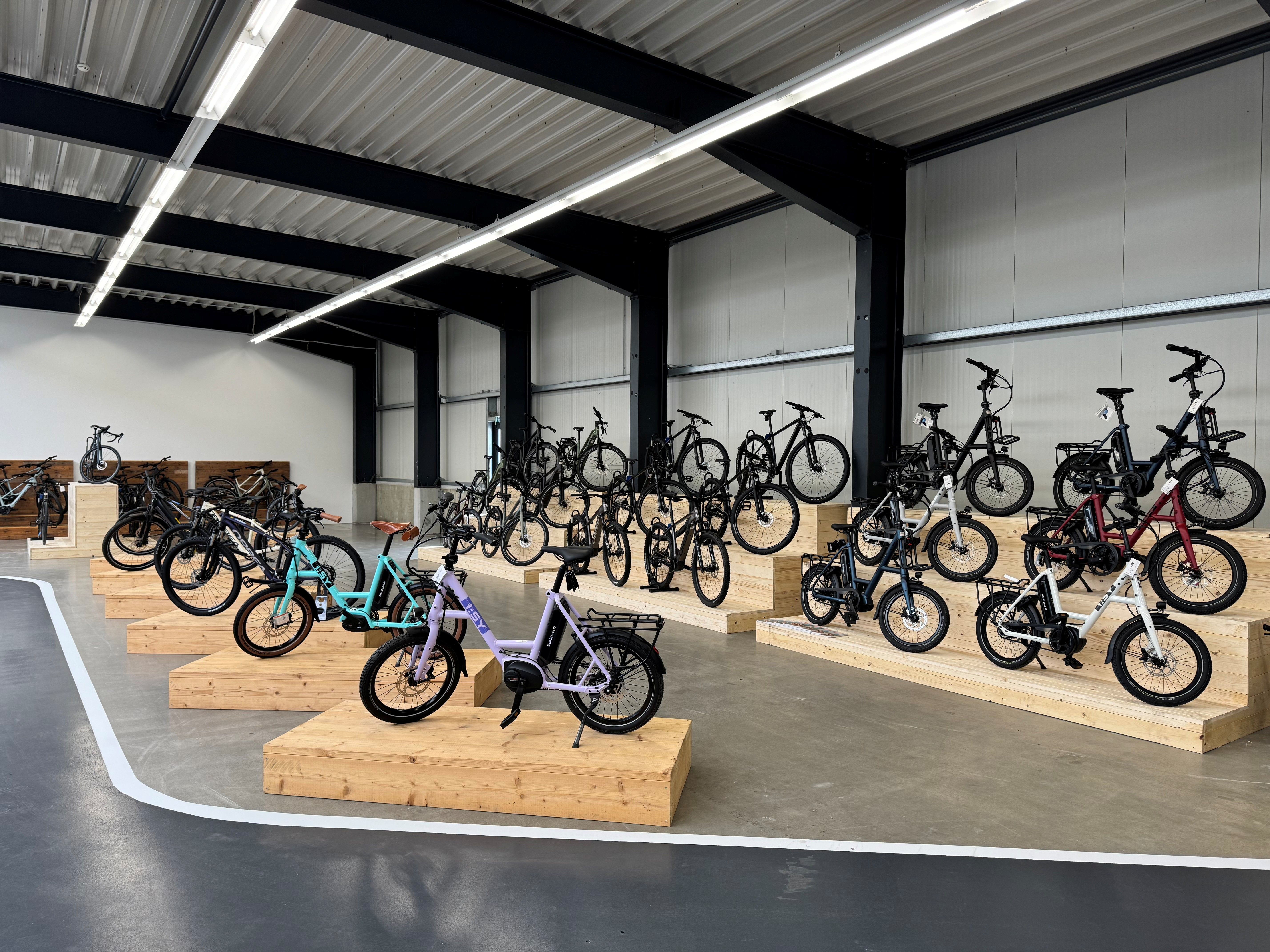 Fahrräder auf Holzpodesten in einem modernen Ausstellungsraum mit Metallträgern und Betonboden.