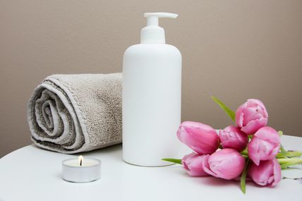 Ein weißer Seifenspender, ein gerolltes Handtuch, eine brennende Kerze und rosa Tulpen auf einem Tisch schaffen eine entspannende Atmosphäre.