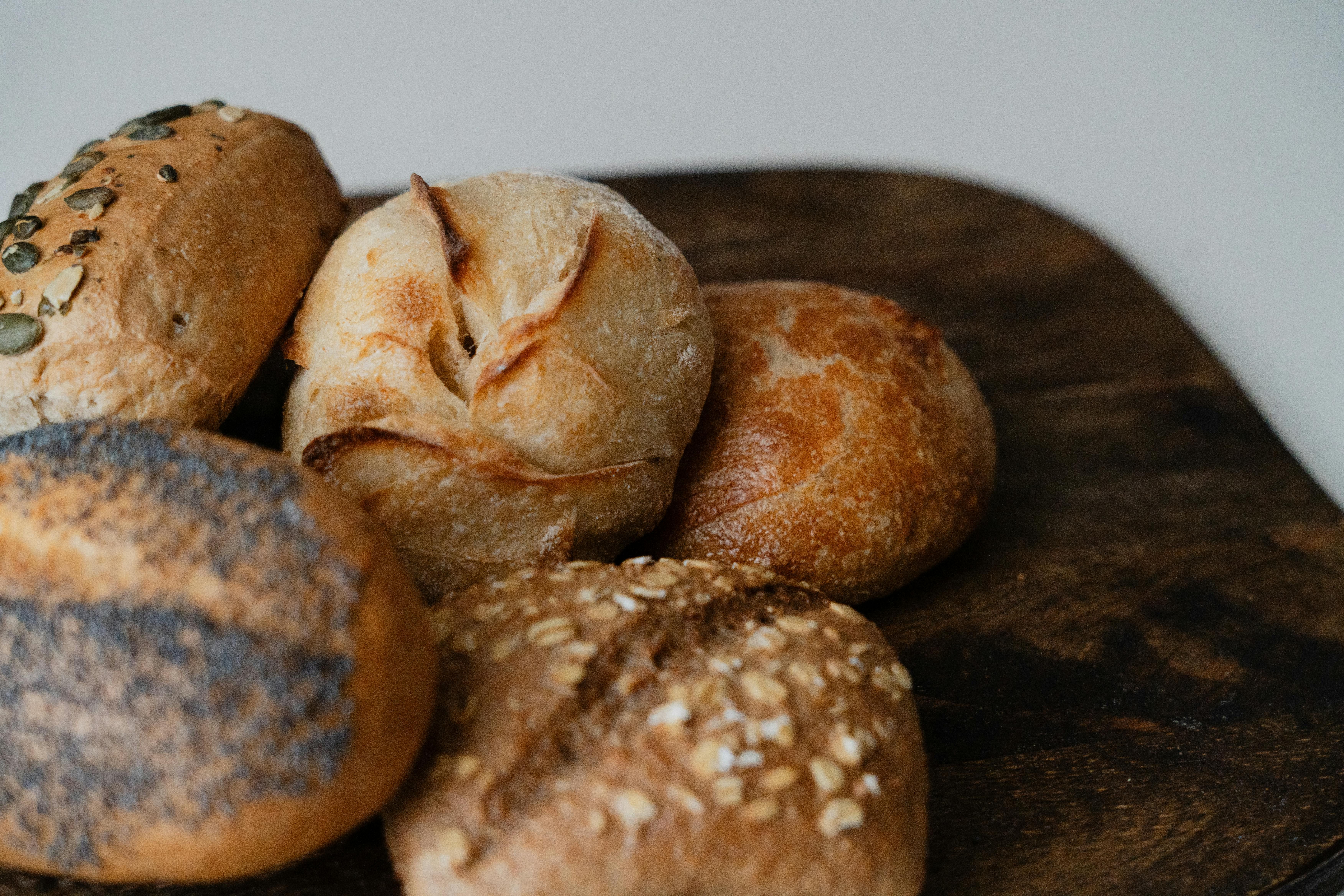 Eine Auswahl an Brötchen, darunter mit Mohn, Körnern und Kürbiskernen, auf einem dunklen Holzbrett arrangiert.