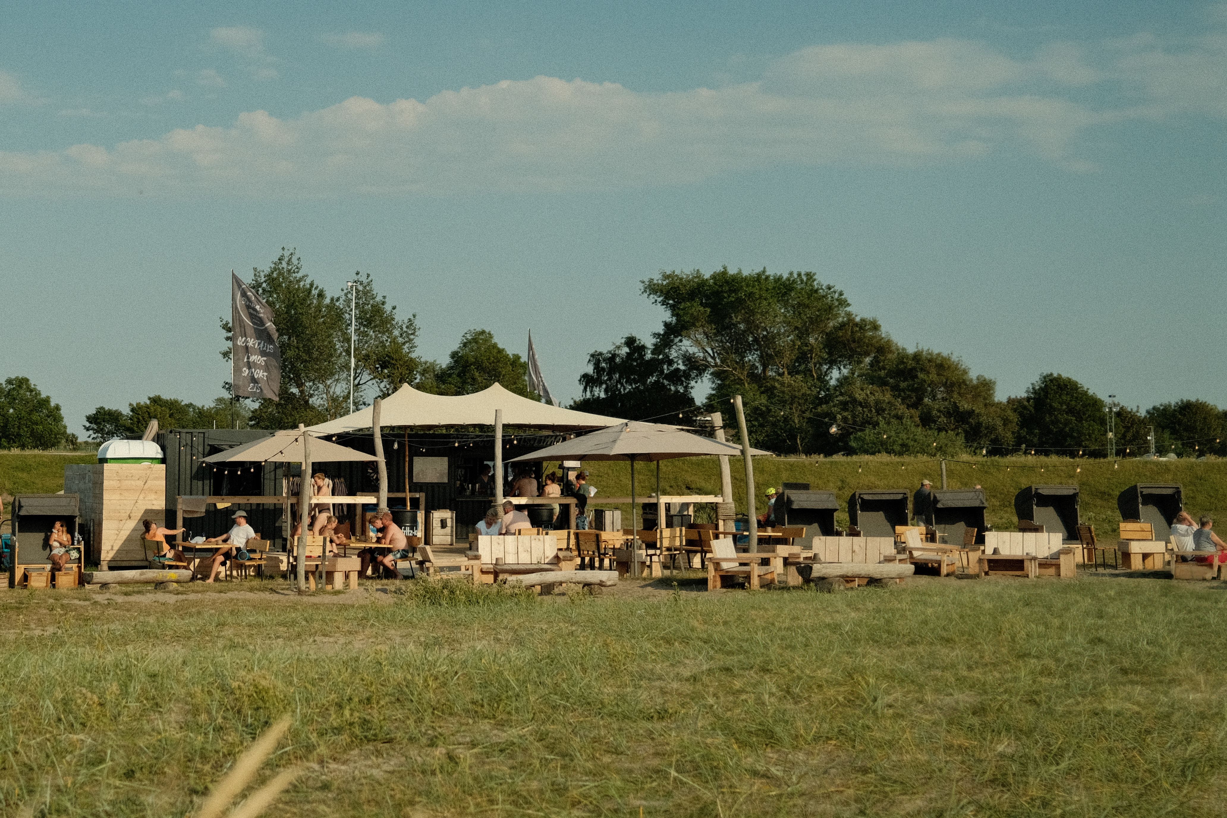 Die Strandbar Strukkamp bietet eine entspannte Atmosphäre mit Sonnensegeln und Sitzgelegenheiten im Freien, umgeben von grüner Landschaft.
