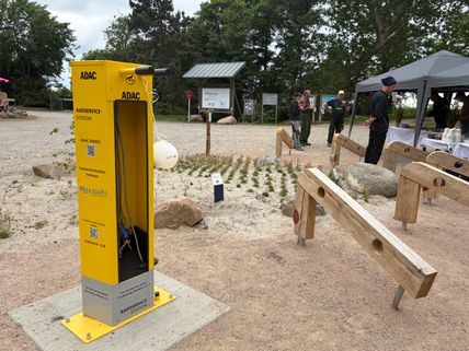 Eine gelbe ADAC Radservicestation steht auf einem Platz. Im Hintergrund sind Personen und ein Pavillon zu sehen.